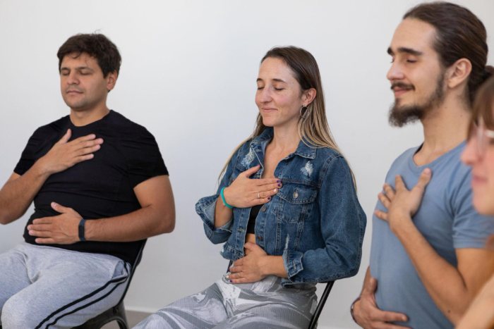 Three people sit with their eyes closed, one hand resting on the chest.
